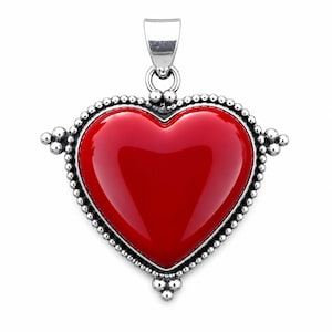 May include: A heart-shaped pendant featuring a smooth, glossy red center stone set within a polished silver frame. The silver border is decorated with a beaded texture, and the piece includes a silver bail at the top for attachment to a chain.