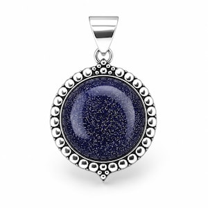 May include: A circular pendant featuring a dark blue, glittery sandstone cabochon set in a polished silver frame. The frame is decorated with a beaded border and a pointed bottom detail, topped with a smooth, triangular silver bail for hanging.