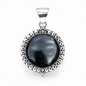 May include: A circular pendant featuring a smooth, polished black stone set in a silver frame. The frame is decorated with a border of small, raised silver spheres and includes a polished silver bail at the top for attachment to a chain.