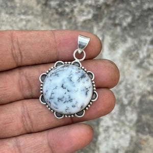 May include: A round pendant with a white stone featuring black dendritic patterns, set in a silver-colored metal frame. The pendant has a decorative scalloped edge and a silver bail for a chain.