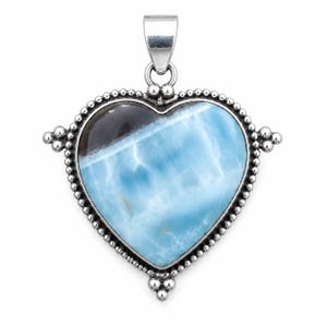 May include: A heart-shaped pendant featuring a polished blue and white Larimar stone with a dark brown inclusion. The stone is set in a silver frame decorated with a beaded border and small silver spheres at the sides and bottom, with a silver bail.