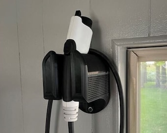 May include: A black electric vehicle charging station with a white charging cable attached to a wall mount. The charging station is mounted near a window with a view of green grass.