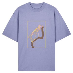 Könnte beinhalten: Ein hellviolettes T-Shirt mit Rundhalsausschnitt und kurzen Ärmeln. Das Shirt zeigt eine rechteckige Grafik eines Skeletts, das sich auf einem Ast ausruht, gelb umrandet. Das Skelett ist in Gelb- und Rosatönen gehalten, der Ast ist braun.
