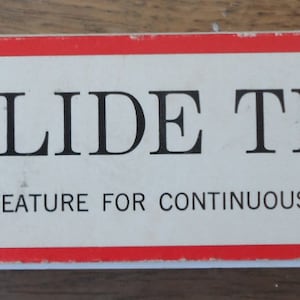 May include: A red and white box with the text "Sears 40-SLIDE TRAY" and "END-LOCK FEATURE FOR CONTINUOUS SHOWINGS". The box is for a slide tray that is compatible with various projectors, including Sears Automatic, Anscomatic, Bell & Howell, Sawyers, and TDC.