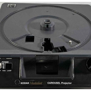 May include: Black Kodak Medalist 4 Carousel Projector with a round slide tray, forward and reverse buttons, power, fan, and lamp controls, and a focus knob.