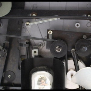May include: Close-up of the inner workings of a vintage cassette player. The image shows a series of gears, belts, and springs that work together to play audio tapes.