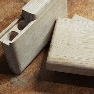 Op de afbeelding: Twee onafgewerkte houten dozen, een met een rechthoekige opening en twee kleinere openingen, de andere met een glad oppervlak. De dozen zijn gemaakt door OneManOnly, een handgemaakt bedrijf.