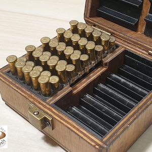 Op de afbeelding: Een houten doos met een scharnierend deksel, met rijen gouden patronen. De doos is gemaakt van lichtbruin hout met een donkerbruine vlek. De doos heeft een klein metalen slot aan de voorkant.