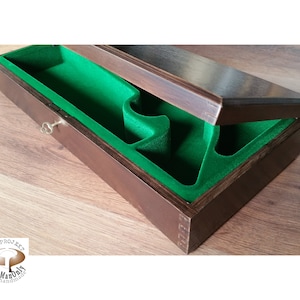 Puede incluir: Una caja de madera con un forro de fieltro verde y una cerradura. La caja está abierta y la tapa está levantada. La caja está hecha de madera oscura y tiene un diseño simple.