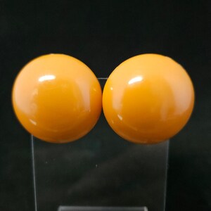 May include: A pair of round, smooth, orange stud earrings with a glossy finish. The earrings are spherical in shape and feature a solid, vibrant orange color throughout, reflecting light on their curved surfaces to create a bright highlight.