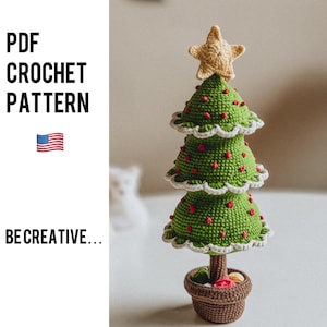 Puede incluir: Un adorno de árbol de Navidad tejido a crochet con una estrella en la parte superior y detalles rojos y blancos. El árbol está sentado en una maceta marrón con un patrón rojo y blanco.