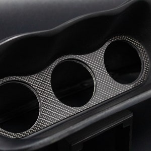 May include: Black plastic car gauge pod with three circular openings for gauges. The pod has a carbon fiber pattern.
