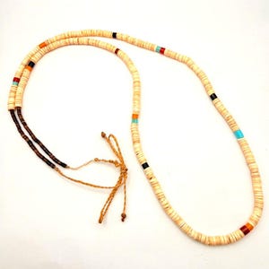May include: A long necklace composed of small, flat, circular off-white beads. The strand is accented with occasional segments of black, turquoise, orange, and red beads. One end features a section of dark brown beads and thin, knotted tan cord.