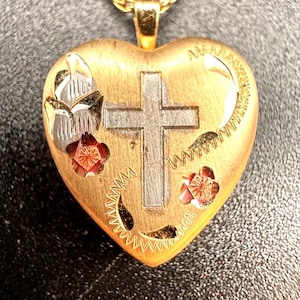 May include: A heart-shaped gold pendant featuring a central silver-toned cross, engraved floral accents, and a curved vine-like pattern. The surface has a brushed gold finish with polished silver details and the word AWARENESS etched at the top.