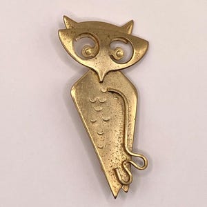 以下が含まれることがあります： ヴィンテージのゴールドトーンのフクロウのブローチ。ブローチは、大きく、様式化された目と、湾曲した装飾的な尾を持つフクロウのデザインが特徴です。フクロウの体は、一連の曲線を持つテクスチャ加工された表面を持っています。クラシックなアクセサリーです。