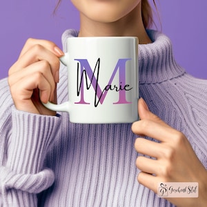 Könnte beinhalten: Weiße Keramiktasse mit einem lila und pinkfarbenen Ombre-Buchstaben "M" und dem Wort "Marie" in schwarzer Schrift.