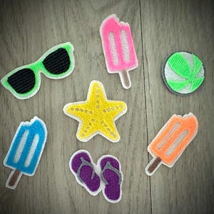 May include: A collection of seven embroidered patches featuring summer themes: neon green sunglasses with black lenses, a pink popsicle, a green and white beach ball, a yellow starfish, a blue popsicle, purple flip-flops, and an orange popsicle.
