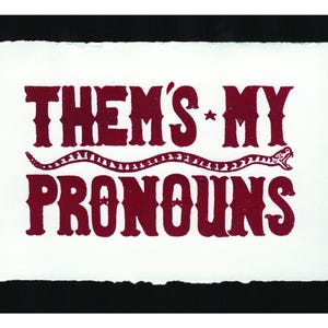 May include: A white card with a red snake and the text "Them's My Pronouns" in a bold, vintage font.