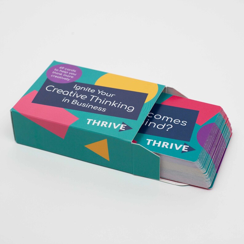 Może przedstawiać: Turkusowe pudełko z kolorowymi kształtami geometrycznymi i tekstem "Ignite Your Creative Thinking in Business" i "THRIVE". Pudełko zawiera stos kart z tekstem "comes ind?" i "THRIVE".
