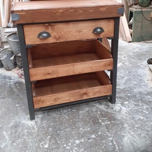May include: A wooden countertop with a drawer and three open shelves on a black metal frame. The countertop is made of reclaimed wood and has a rustic look. The shelves are ideal for storing kitchen supplies or other items.