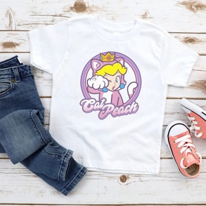 May include: White t-shirt with a pink and purple graphic of a cat wearing a crown and the text "Cat Peach".