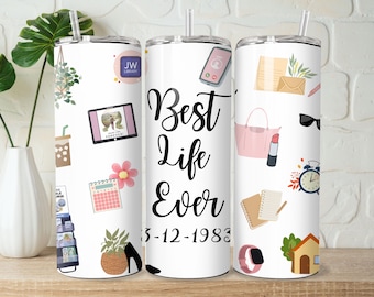 May include: White tumbler with a black and white design featuring the text "Best Life Ever" and the date "3-12-1983". The tumbler is decorated with various illustrations including a calendar, a house, a purse, a lipstick, sunglasses, a book, a plant, a shoe, and a phone.