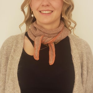 Puede incluir: Una mujer con un cárdigan marrón y una blusa negra con una bufanda de punto rosa y naranja atada alrededor del cuello.