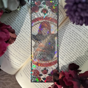 Könnte beinhalten: Rechteckiger Lesezeichen mit einem Buntglasdesign mit einer Frau mit rotem Haar und einem detaillierten Outfit. Das Lesezeichen hat ein holografisches Finish und ist von roten Rosen und Text umrahmt.