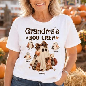 May include: A white t-shirt featuring the brown text Grandma's BOO CREW. The graphic includes a large central ghost with a leopard print bow and patchwork details, surrounded by three smaller ghosts labeled Henry, Charlie, and Sophia.