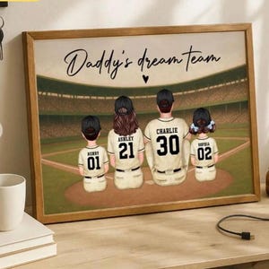 Pode incluir: Obra de arte emoldurada com tema de beisebol. A imagem mostra uma família de quatro pessoas em camisas de beisebol com o texto "Daddy's dream team". Cada camisa tem um nome e um número. O fundo retrata um campo de beisebol.