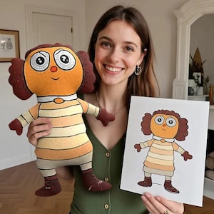 May include: A plush doll with a cartoonish design, featuring a round head, large eyes, and striped clothing in shades of orange and beige. The doll is held next to a drawing of the same character. The doll has brown hair and shoes.