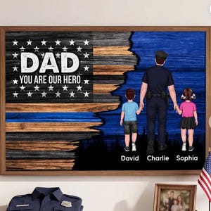 May include: A framed artwork featuring a stylized American flag design with the words "DAD YOU ARE OUR HERO." The artwork depicts a police officer holding hands with two children. The children's names are David, Charlie, and Sophia.