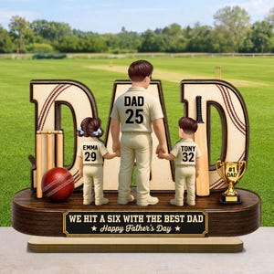 May include: A Father's Day cricket-themed figurine. The word "DAD" is prominently displayed, with a father figure holding hands with two children. The figurine includes a cricket ball, bat, and a trophy that says "#1 DAD". The base reads "WE HIT A SIX WITH THE BEST DAD Happy Father's Day".