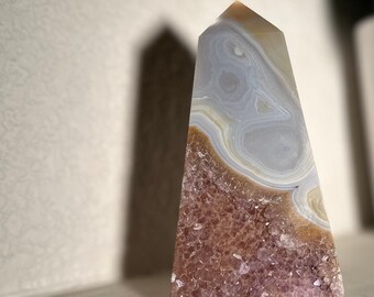 May include: A large, clear, and white agate crystal point with a base of purple amethyst crystals. The crystal is shaped like a pyramid and has a smooth, polished surface.