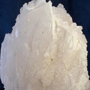 May include: A large, jagged cluster of translucent white quartz crystals. The mineral specimen features sharp, angular edges and a rough, crystalline texture with varying degrees of opacity throughout the formation, creating a bright, multifaceted appearance.