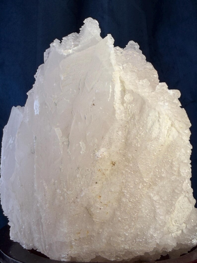 May include: A large, jagged cluster of translucent white quartz crystals. The mineral specimen features sharp, angular edges and a rough, crystalline texture with varying degrees of opacity throughout the formation, creating a bright, multifaceted appearance.