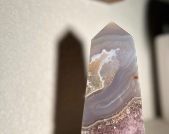 May include: A purple, white, and brown agate crystal point with a pointed top and a flat base. The crystal has a natural, rough texture and is a popular choice for crystal healing and meditation.