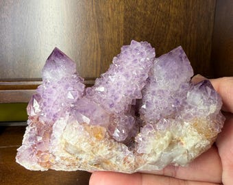 May include: A cluster of amethyst crystals, displaying various shades of purple. The crystals are set on a base with white and tan colours. The image emphasises the natural formation and texture of the gemstones.