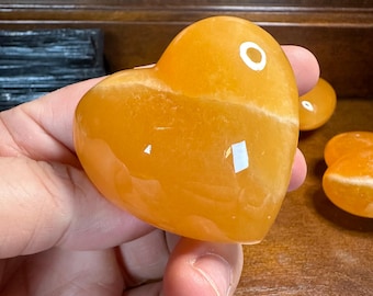 May include: A heart-shaped orange carnelian crystal. The crystal is smooth and polished, with a light orange color.