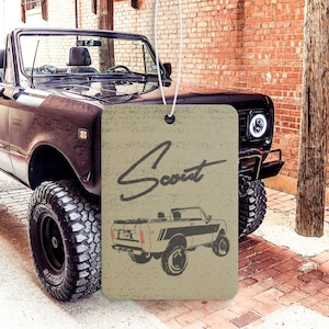 May include: A brown car air freshener with a vintage illustration of a black and white International Scout. The text "Scout" is written in cursive on the air freshener.