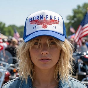 Könnte beinhalten: Weiß-blaue Trucker-Mütze mit der Aufschrift "BORN FREE" und einer Adler-Grafik. Die Mütze trägt auch die Zahlen "17" und "76". Die Person trägt eine Jeansjacke.