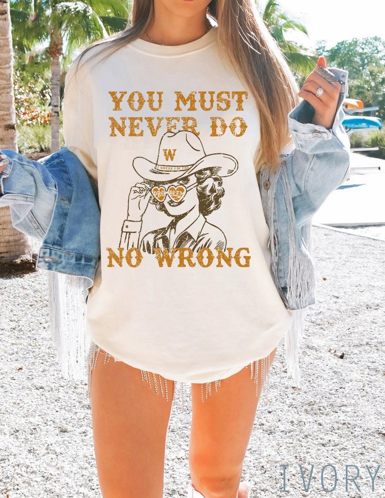 May include: A white t-shirt with the text "You must never do no wrong" and a cartoon image of a woman wearing a cowboy hat and sunglasses. The woman is holding a heart-shaped object with the letter "W" on it.