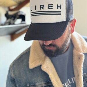 May include: A black and white trucker hat with the word "JIREH" printed in black on the front. The hat has a black mesh back and a white front panel.
