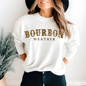 May include: White sweatshirt with brown text that reads "Bourbon Weather".