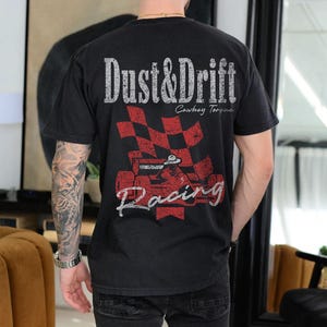 May include: Black t-shirt with a distressed graphic featuring the words "Dust & Drift" above a red and black checkered flag and a race car. The shirt also has the words "Cowboy Torque" and "Racing".