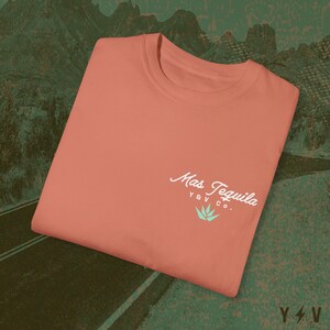 May include: A coral coloured t-shirt with a white logo that says "Mas Tequila Y&V Co." with a green agave plant graphic.