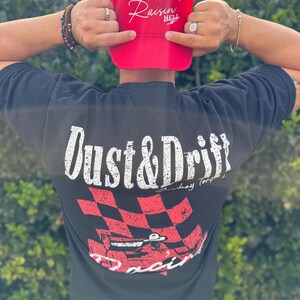 May include: A red trucker hat with the text "Raisin' Hell" in white script. A black t-shirt with "Dust & Drift" in white, and a red and black checkered flag design with a race car.