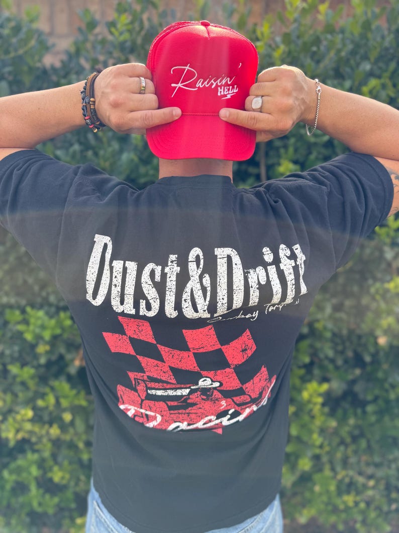 May include: A red trucker hat with the text "Raisin' Hell" in white script. A black t-shirt with "Dust & Drift" in white, and a red and black checkered flag design with a race car.