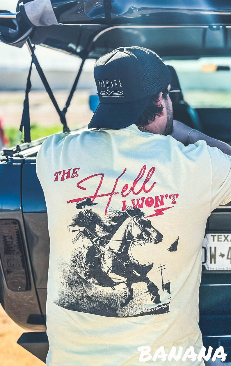 Peut inclure: Un t-shirt beige clair avec une illustration en noir et blanc d'un cow-boy &agrave; cheval. Le texte "THE Hell I WON'T" est imprim&eacute; en rouge sur le t-shirt.