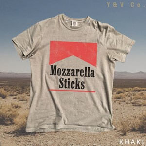 May include: A light grey t-shirt featuring a red and black graphic of a cigarette pack that reads "Mozzarella Sticks". The shirt is made from a soft, comfortable fabric and has a relaxed fit.